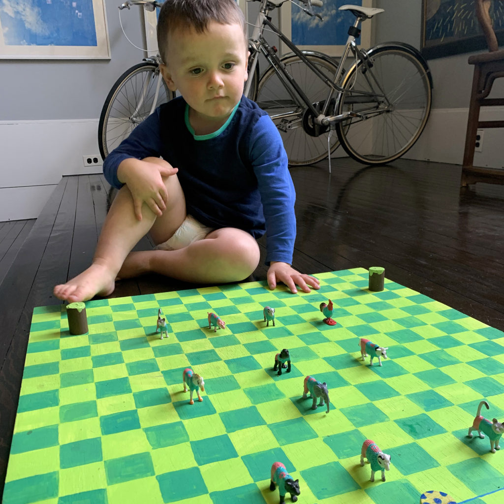 a boy staring at a green checker board with painted animal figurines on it.
