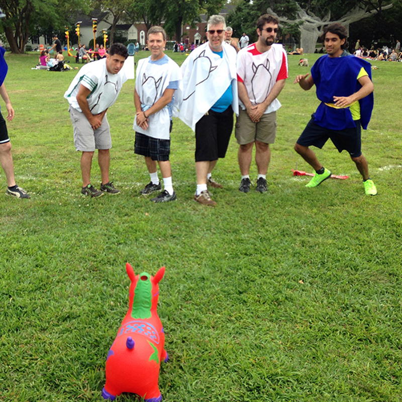 A pink bouncy horse and seven men in uniforms on a green field.