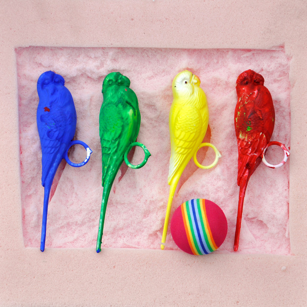 Three painted sculptures of parrots and a ball in rainbow.