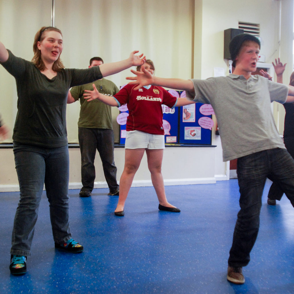 A group of young adults with their arms open, seemingly dancing together, in a classroom.