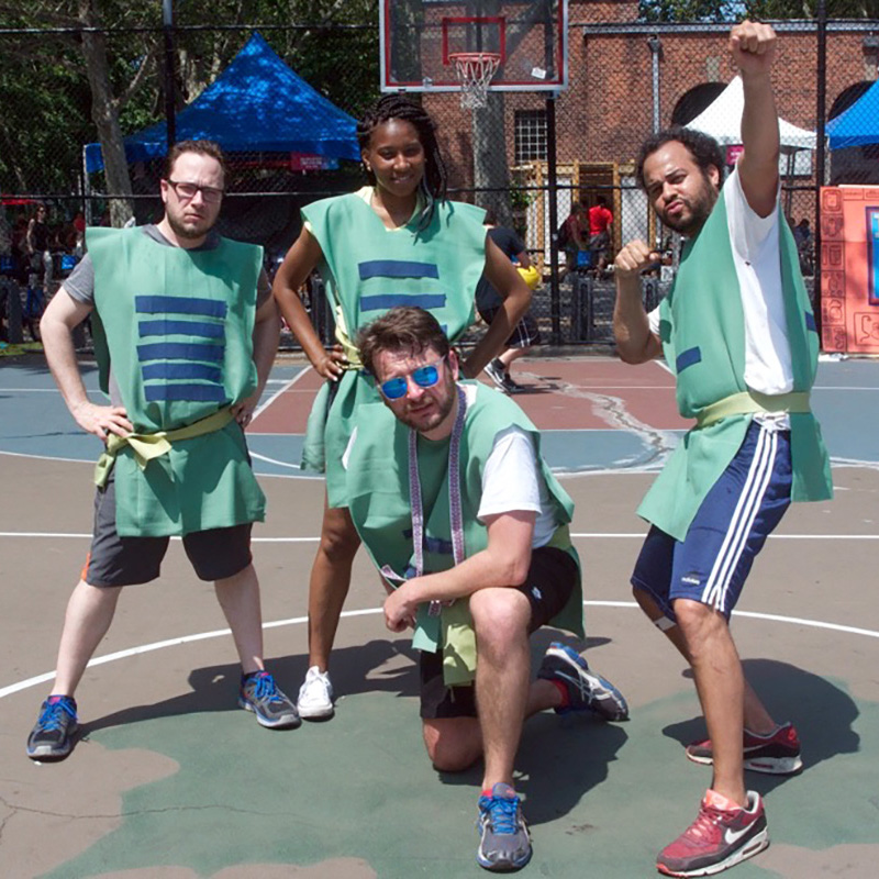 Three men and a woman in a custom green uniform posing for the camera on an outdoor basketball court.